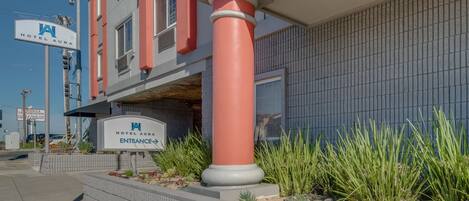 A hotel entrance with a prominent red column, a sign reading "Hotel Aura Entrance," and a landscaped area with plants.