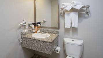 A bathroom with a granite countertop sink, a mirror, a towel rack with towels, a toilet, and a hairdryer.
