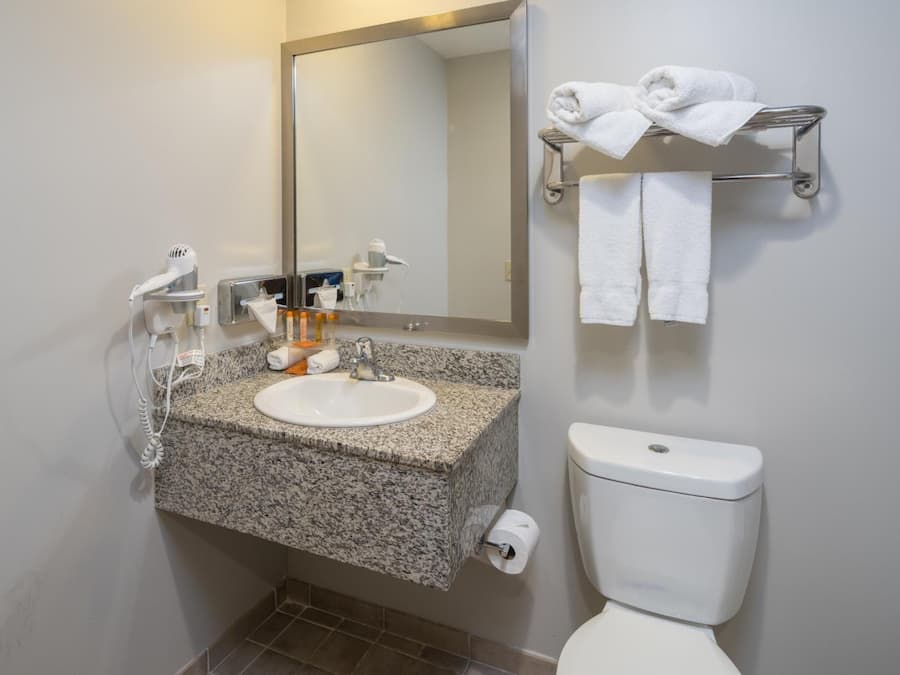 A bathroom with a granite countertop sink, a mirror, a towel rack with towels, a toilet, and a hairdryer.
