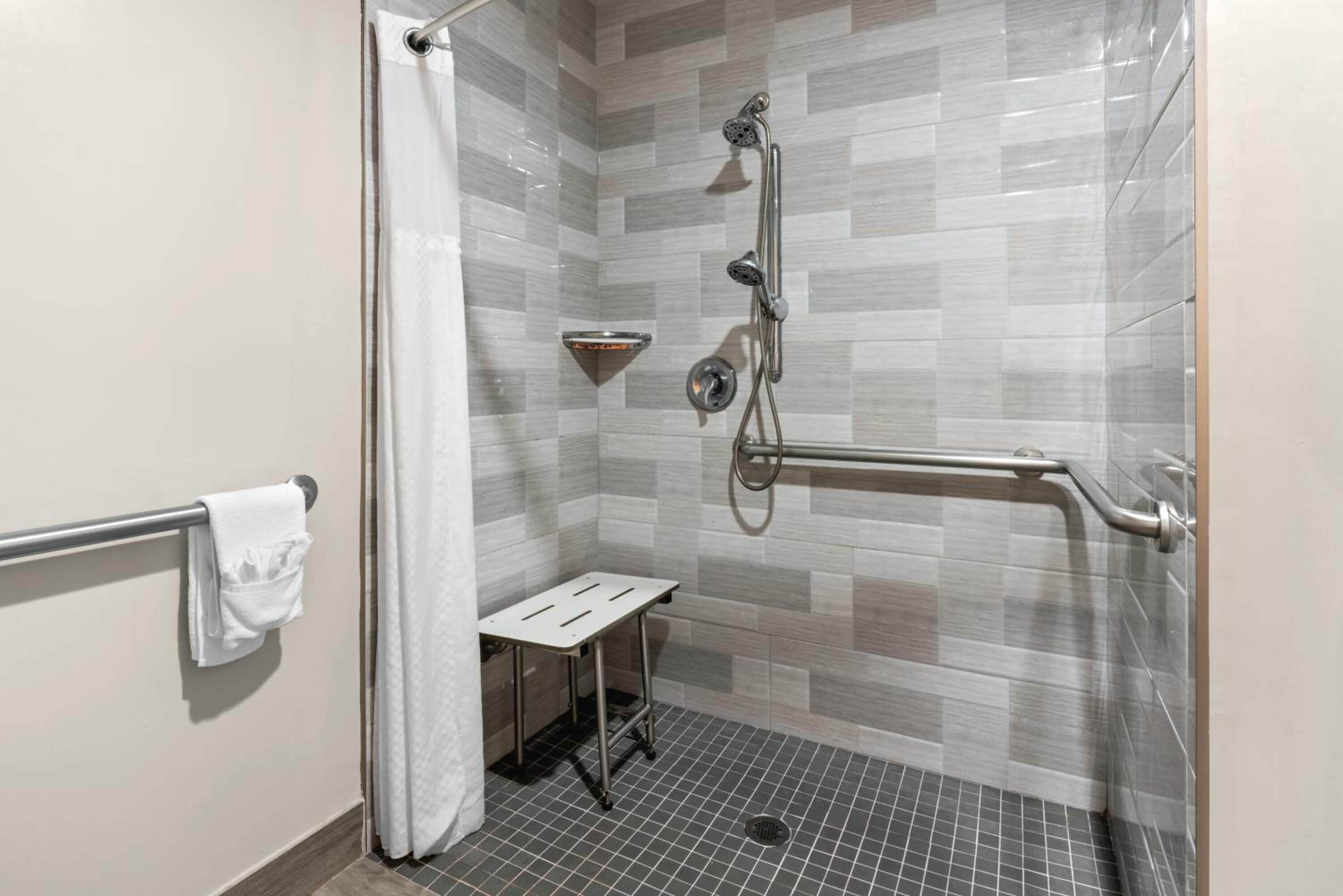 A shower area with a grab bar, a small table, and a towel rack.