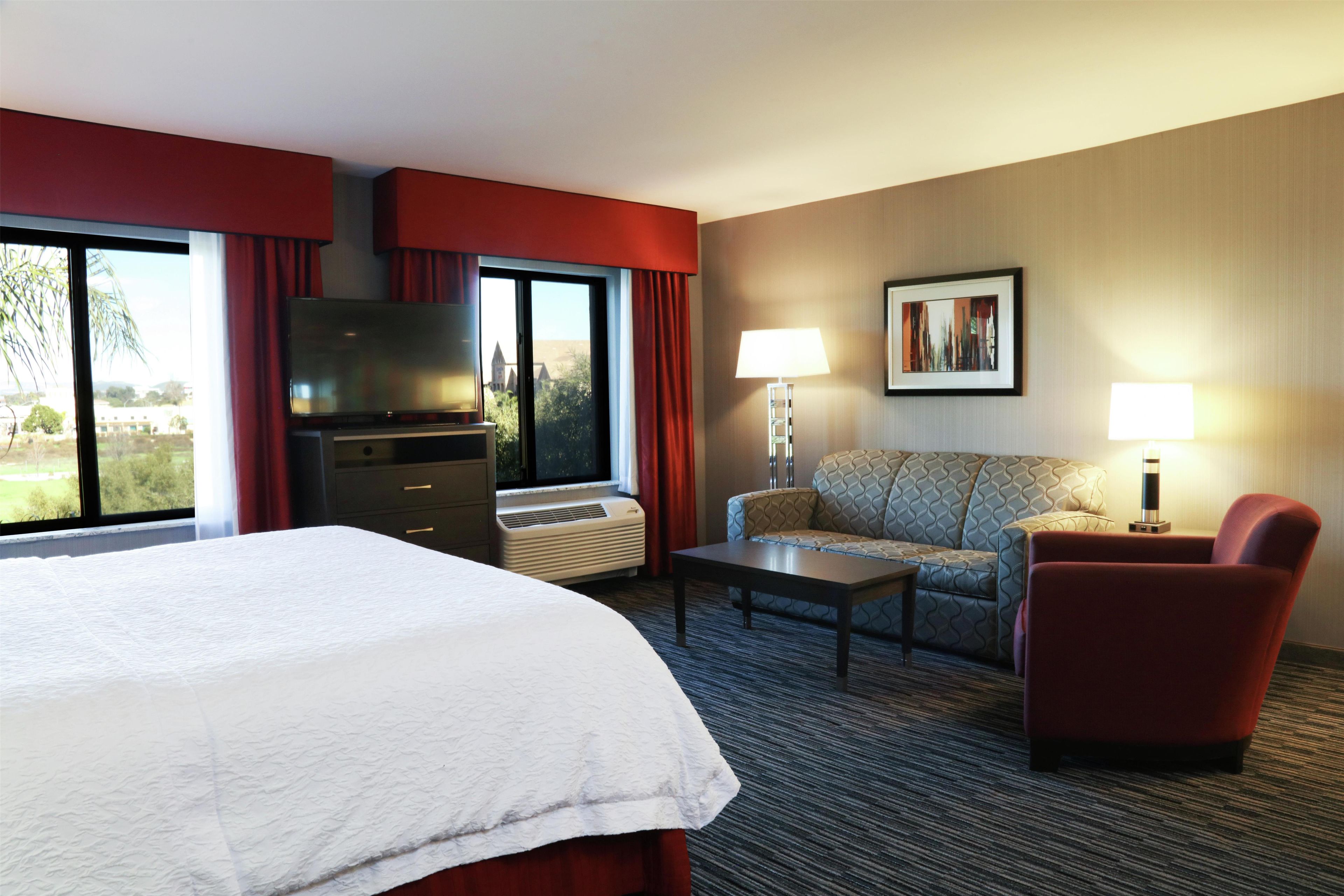 A hotel room with a bed, a television, a sofa, a chair, a coffee table, and a lamp.