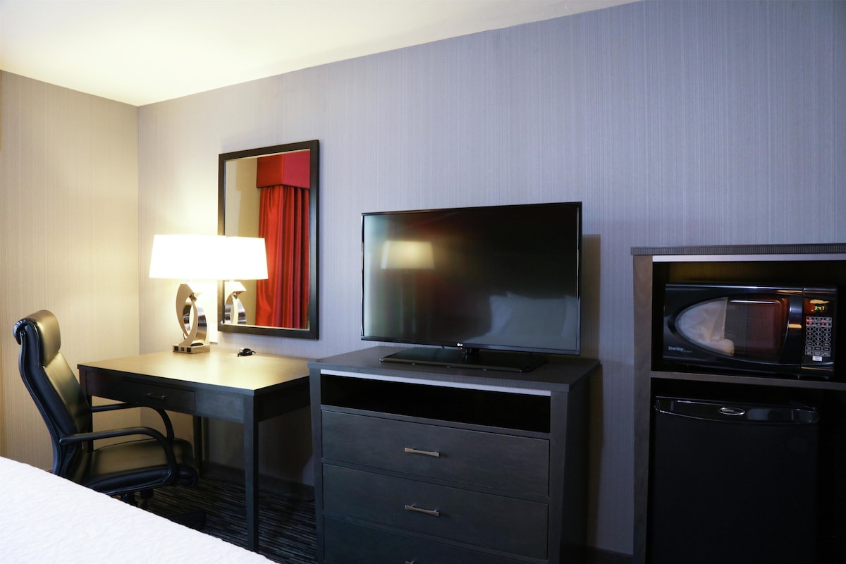Een hotelkamer met een bed, een bureau met een lamp, een televisie, een magnetron en een kleine koelkast.