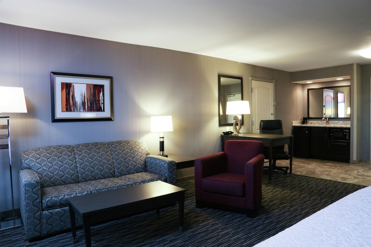 Een hotelkamer met een bank, fauteuil, eettafel en een keukenhoek.
