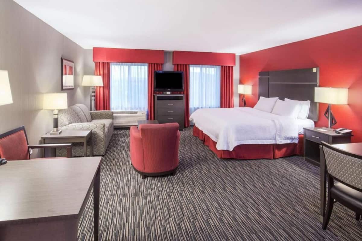 Ein Hotelzimmer mit Bett, Schreibtisch, Sessel, Fernseher und Sofa.
