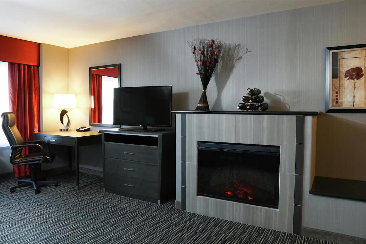 Ein Hotelzimmer mit Schreibtisch, Stuhl, Fernseher, Kamin und Bildern an der Wand.