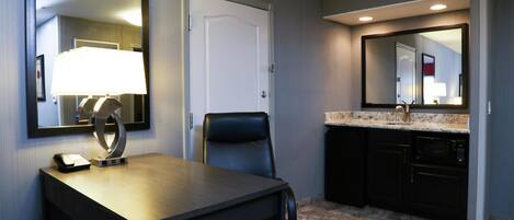 A hotel room with a desk, chair, and a large mirror.