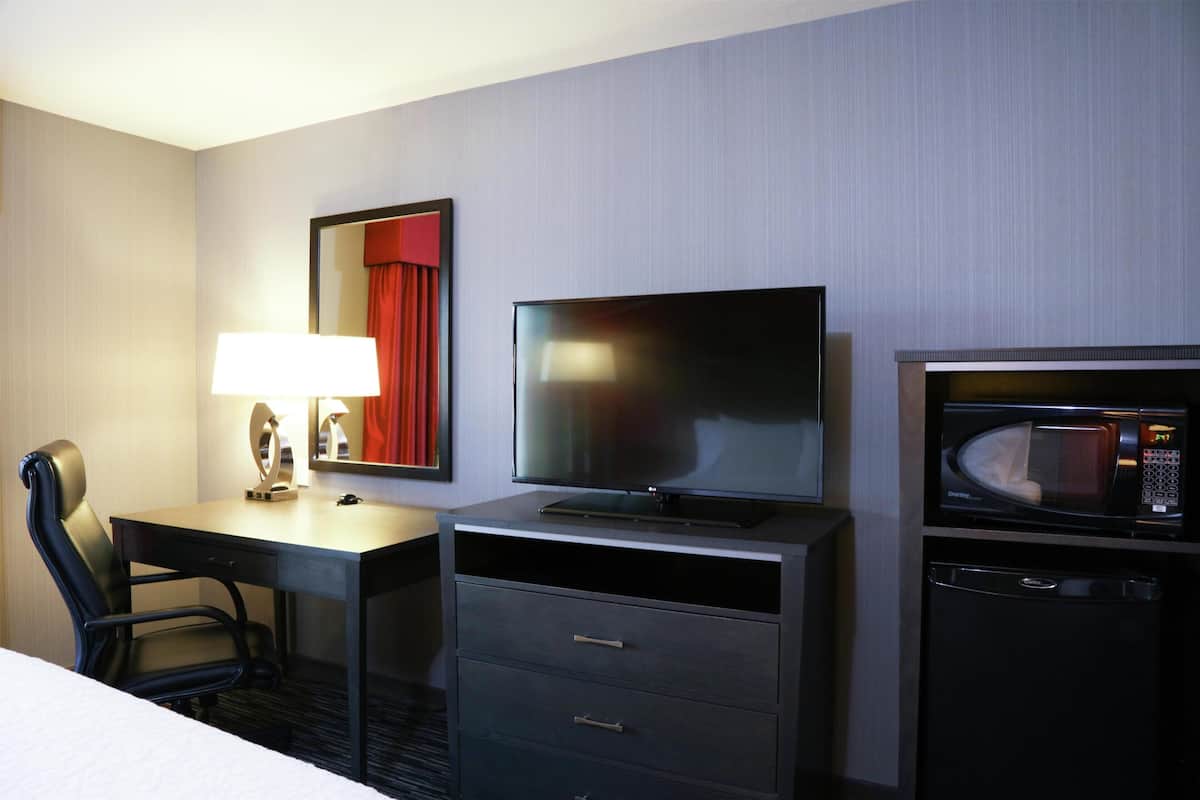 Ein Hotelzimmer mit Bett, Schreibtisch mit Lampe, Fernseher, Mikrowelle und kleinem Kühlschrank.