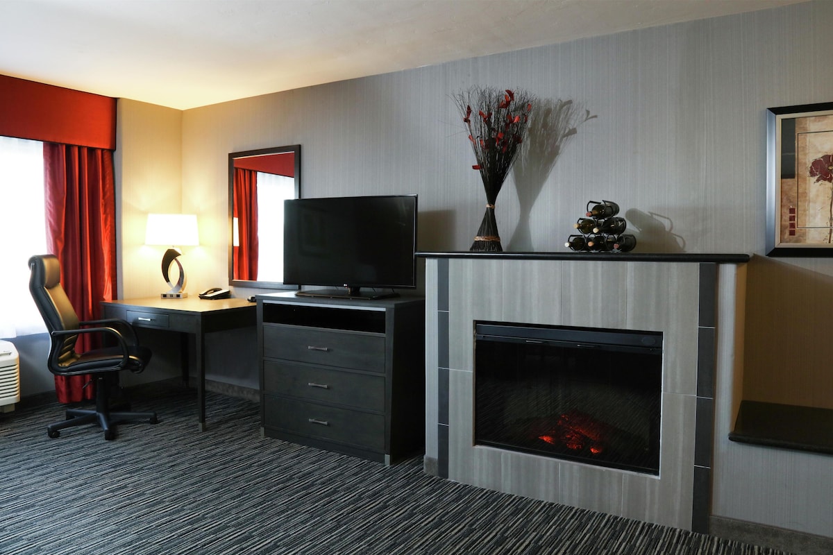 Een hotelkamer met een bureau, stoel, televisie, open haard en kunst aan de muur.
