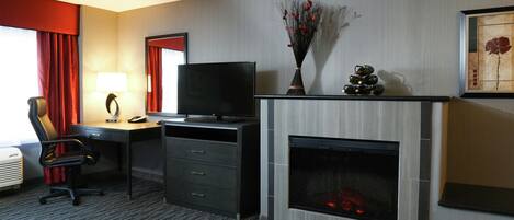 A hotel room with a desk, chair, television, fireplace, and artwork on the wall.