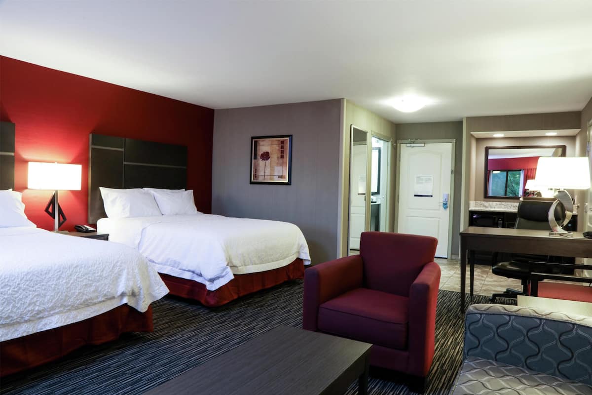 Ein Hotelzimmer mit zwei Betten, einem Schreibtisch, einem Stuhl und einer kleinen Sitzecke.