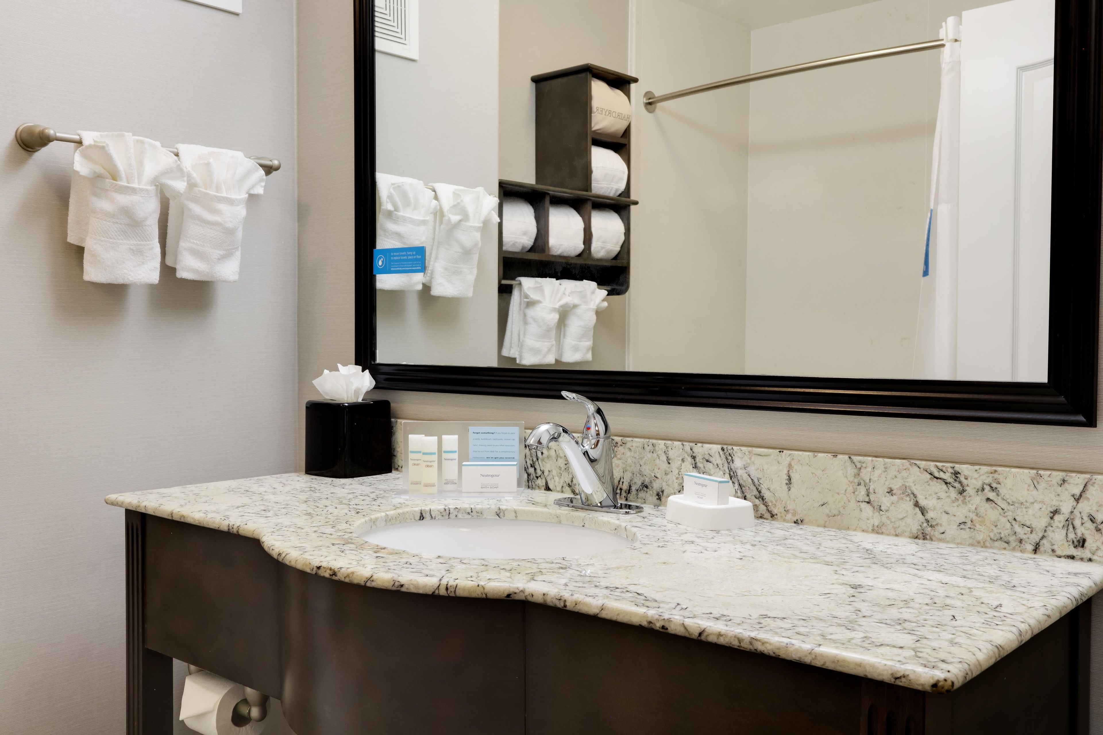 A bathroom with a marble sink, a towel rack, a mirror, and a towel dispenser.