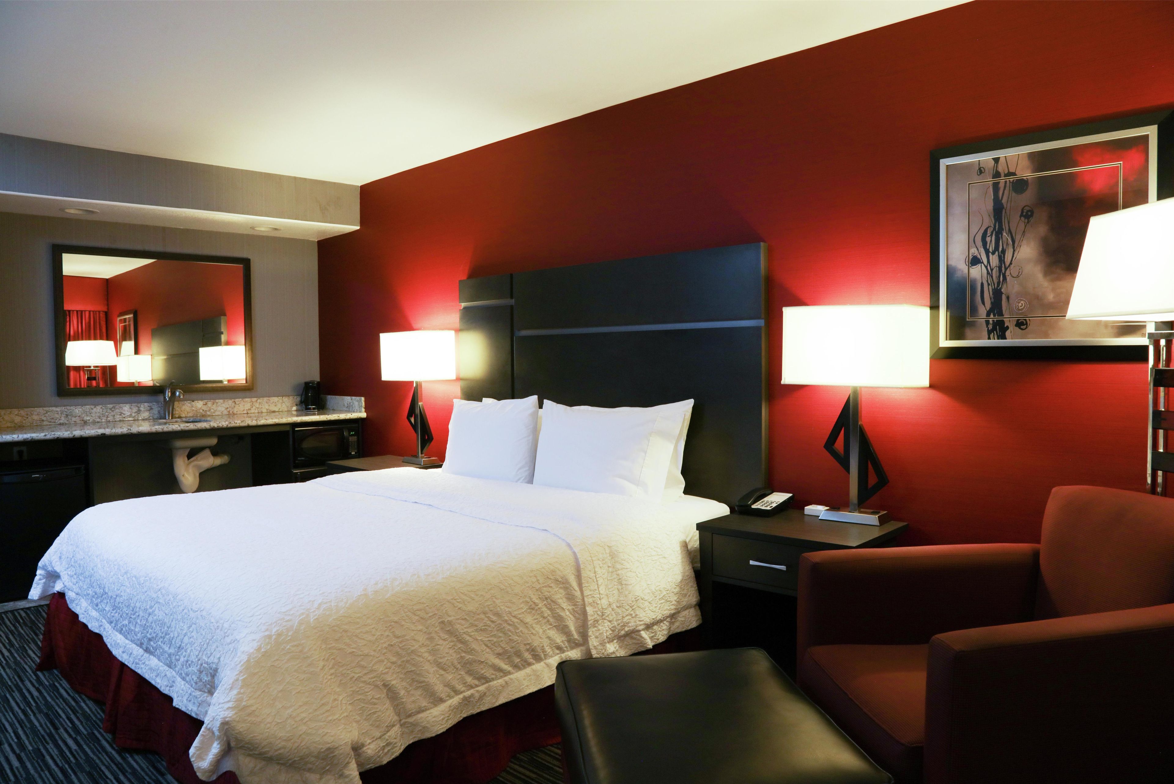 A hotel room with a large bed, a desk with a lamp, a chair, and a painting on the wall.