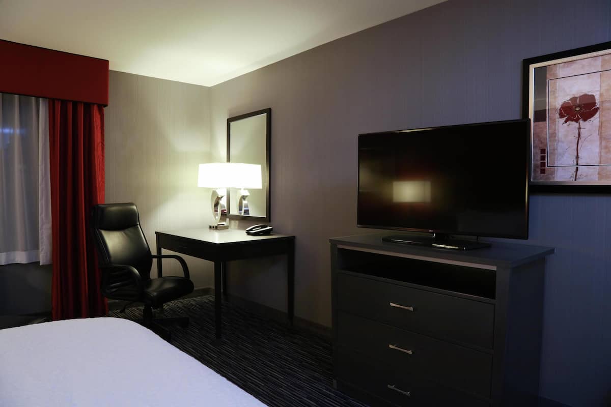 Ein Hotelzimmer mit einem Bett, einem Schreibtisch mit Lampe, einem Fernseher und einem Sessel.