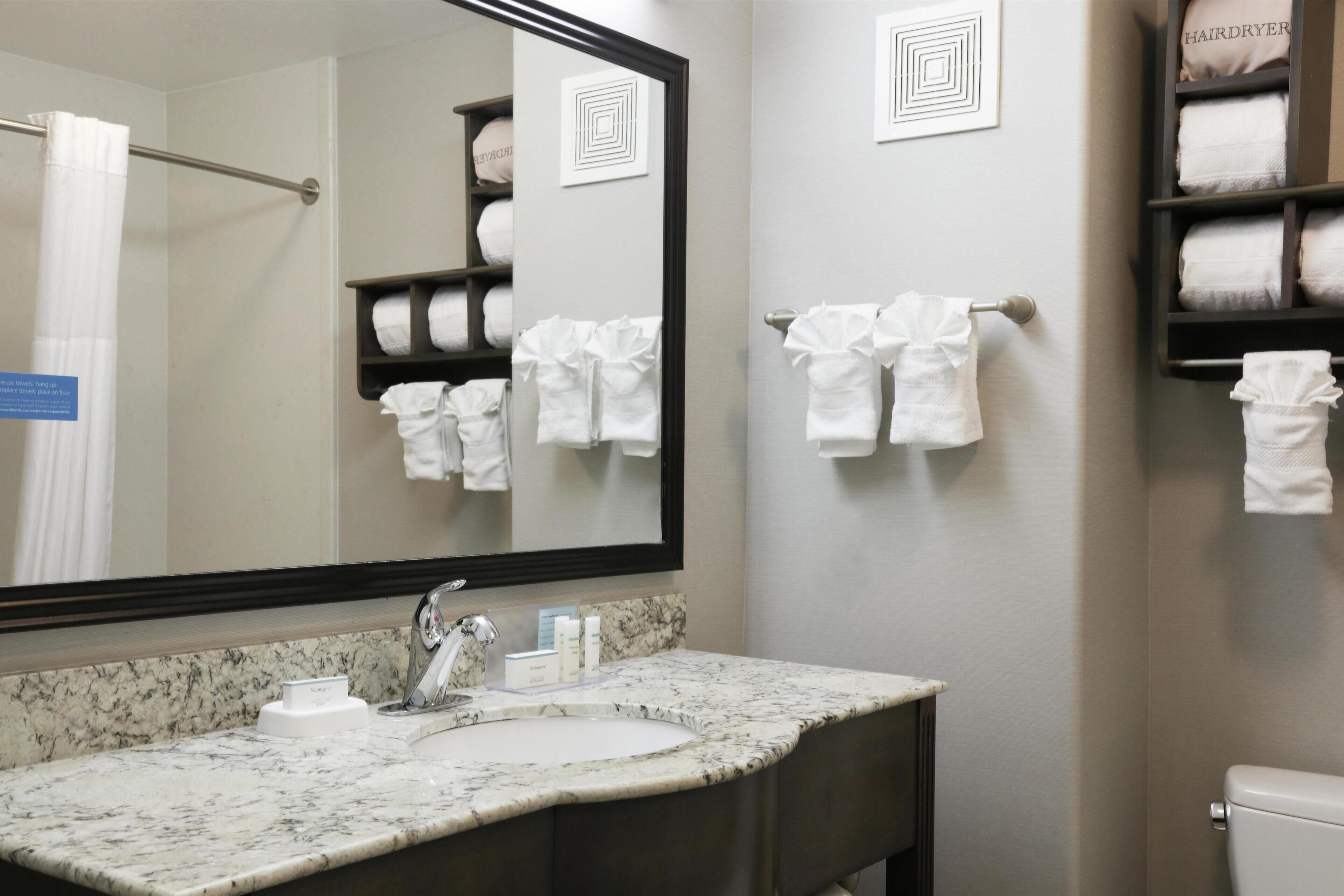 A bathroom with a marble sink, a large mirror, and a towel rack with multiple towels.