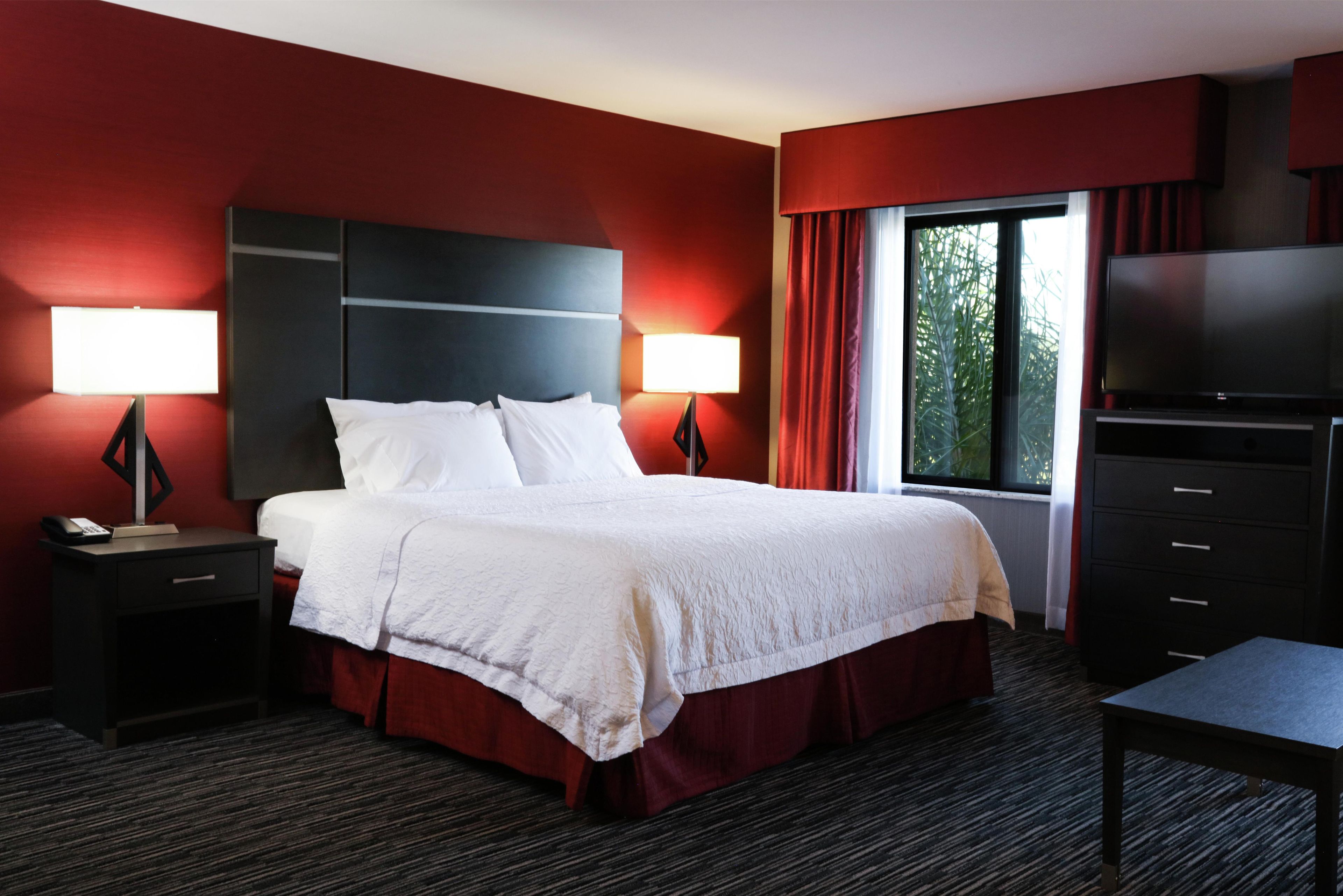 A hotel room with a large bed, two bedside tables with lamps, a TV, and a window with curtains.