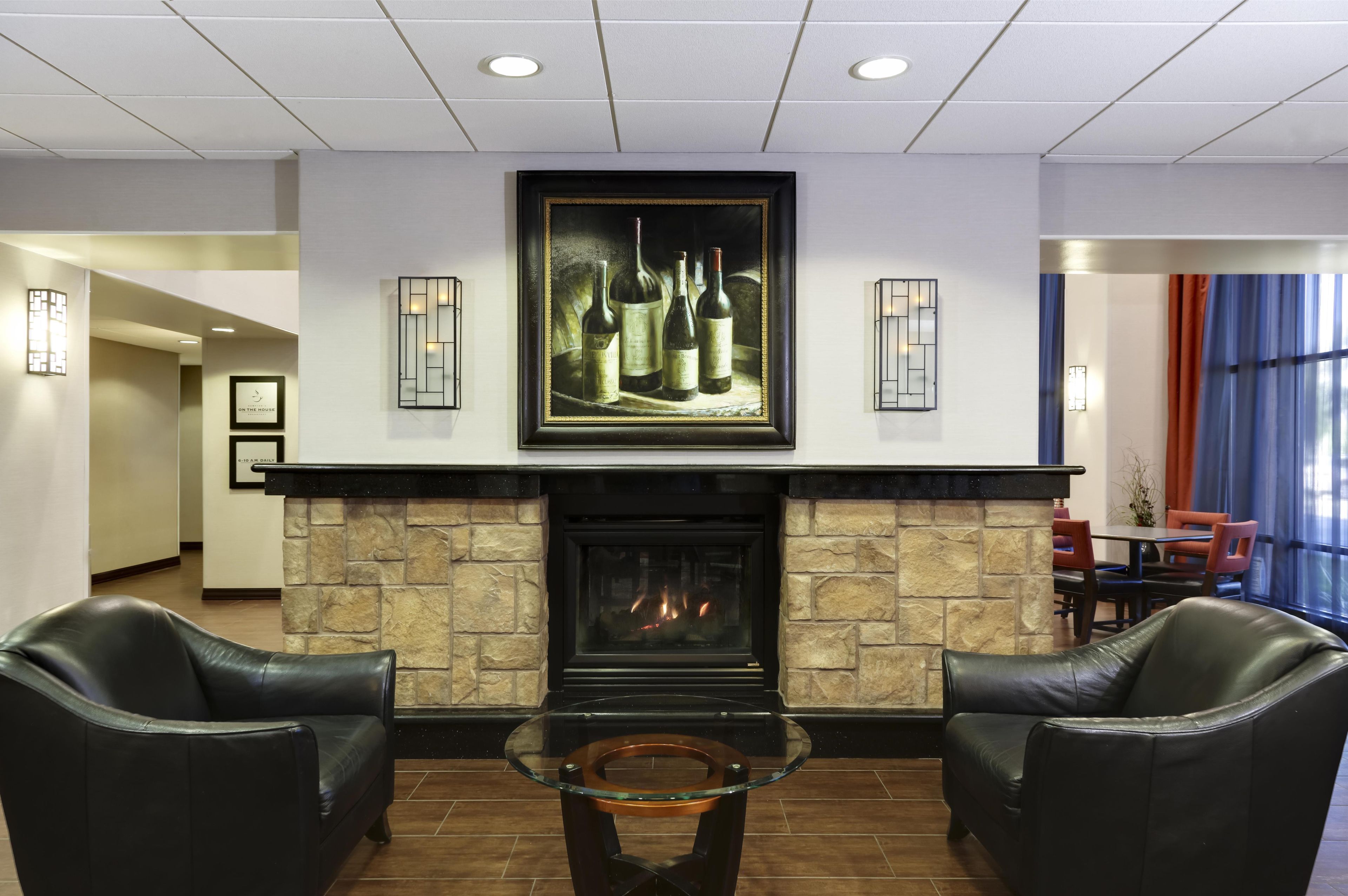 A lobby with a fireplace, framed artwork, leather chairs, and a glass table.