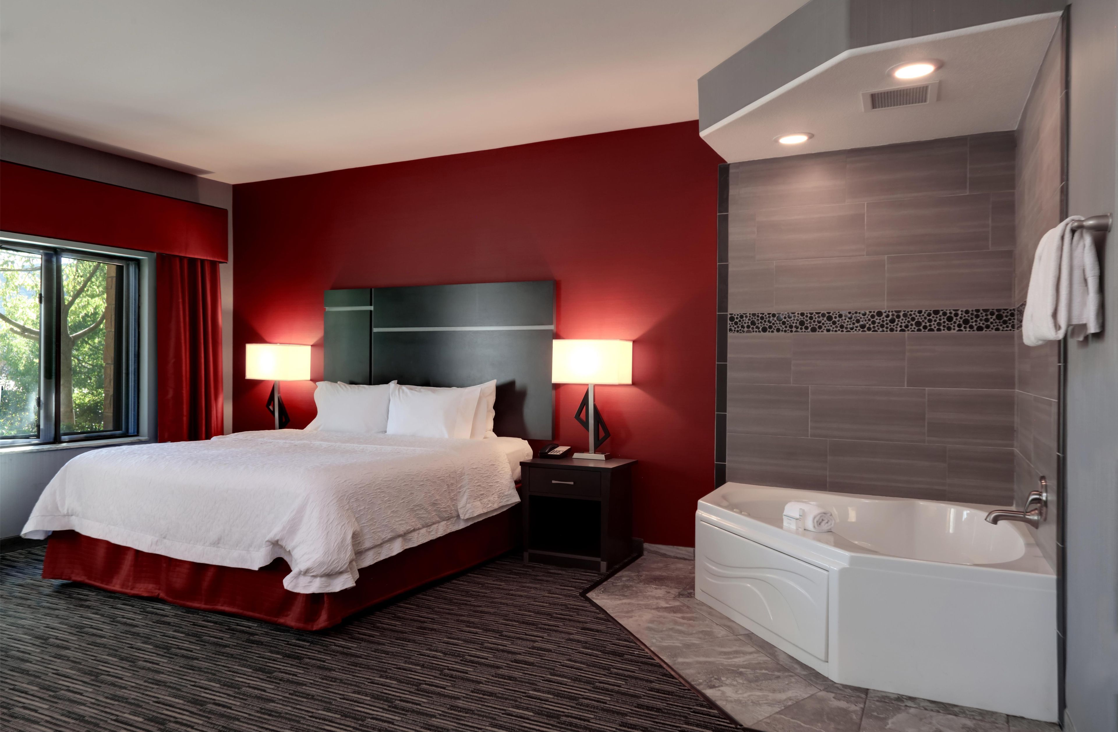 A hotel room with a large bed, bedside lamps, a bathtub, and a window with curtains.