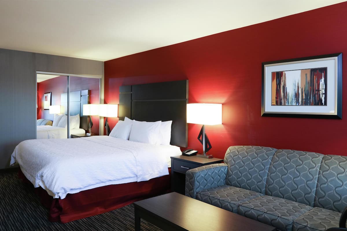 Ein Hotelzimmer mit Bett, Sofa, Schreibtisch, Lampe, Telefon und einem Gemälde an der Wand.