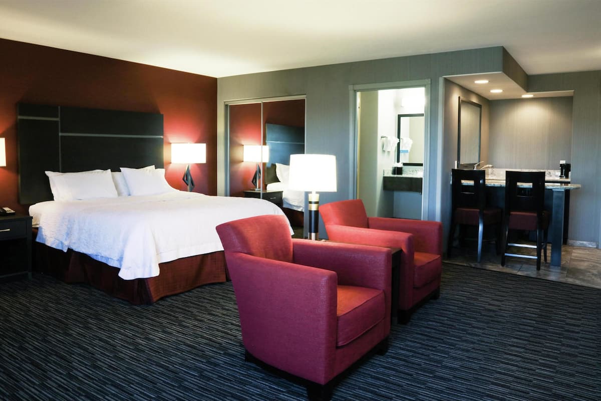Ein Hotelzimmer mit einem Bett, zwei roten Sessel, einem Schreibtisch mit Stuhl und einem Spiegel.