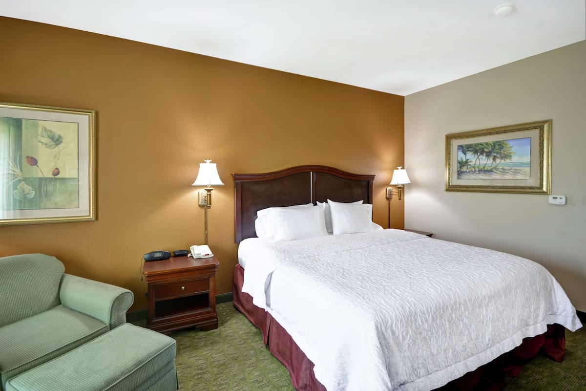 Ein Hotelzimmer mit einem großen Bett, zwei Nachttischlampen, einem Nachttisch, einem Sessel und zwei gerahmten Bildern an den Wänden.