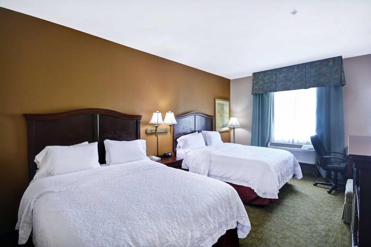 Ein Hotelzimmer mit zwei Betten, einem Schreibtisch, einem Stuhl und einem Fenster mit Vorhängen.