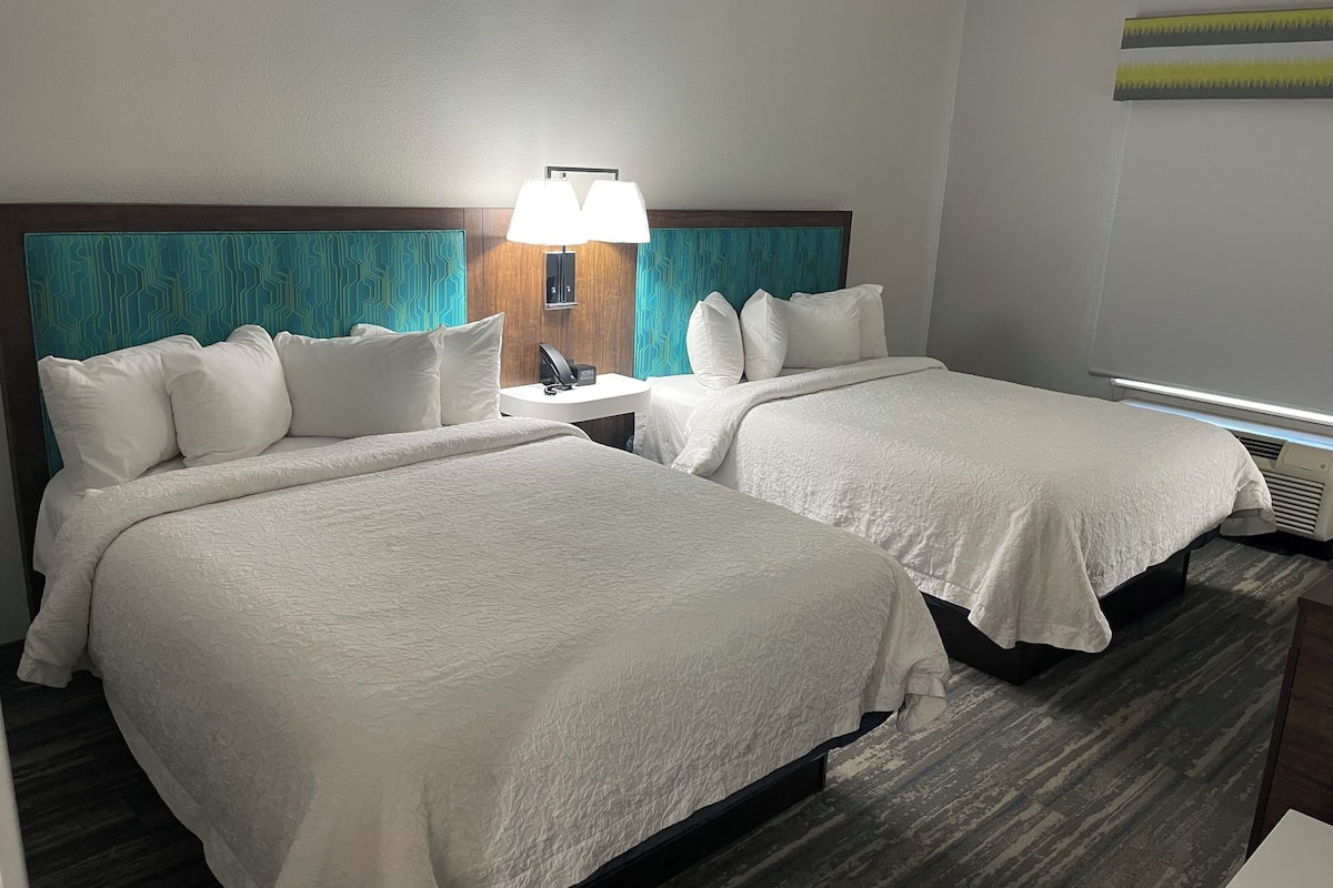 Ein Hotelzimmer mit zwei Betten, einem Nachttisch mit Lampe und einer Wand-Klimaanlage.