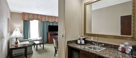 Habitación de hotel con kitchenette, un espejo grande, sofá, televisor y zona de comedor.