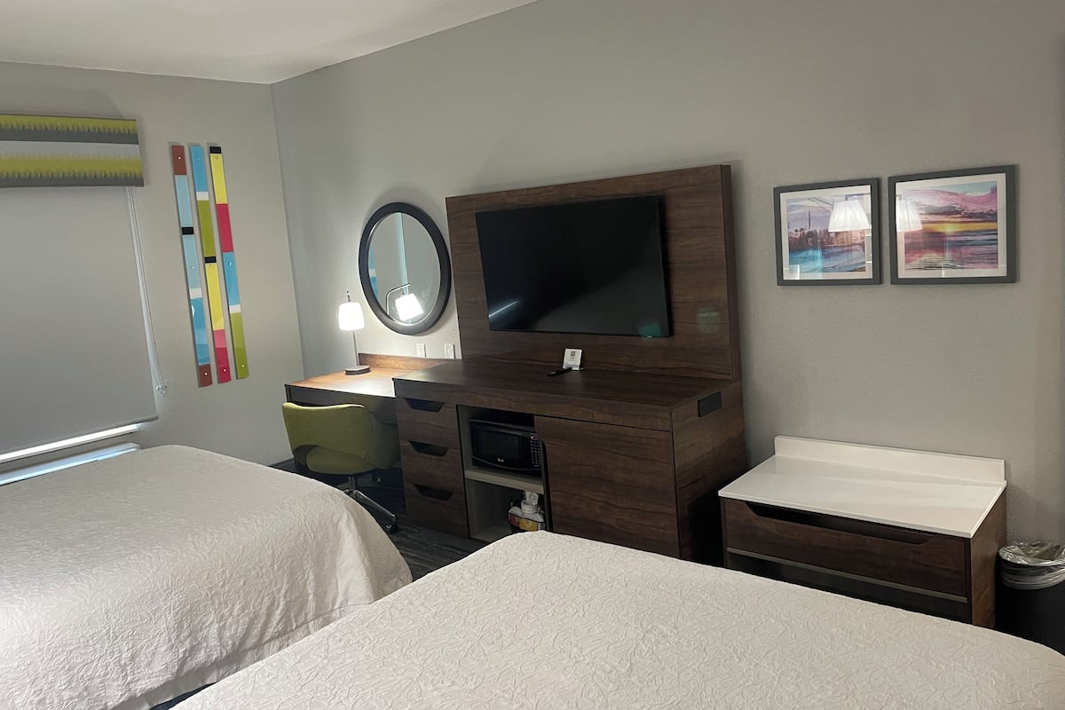 Ein Hotelzimmer mit zwei Betten, einem Schreibtisch mit Fernseher, einem Spiegel und Bildern an der Wand.