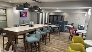A modern dining area with a long communal table, individual seating, and a television screen. - Hampton Inn Corpus Christi-Northwest I-37 (Corpus Christi)
