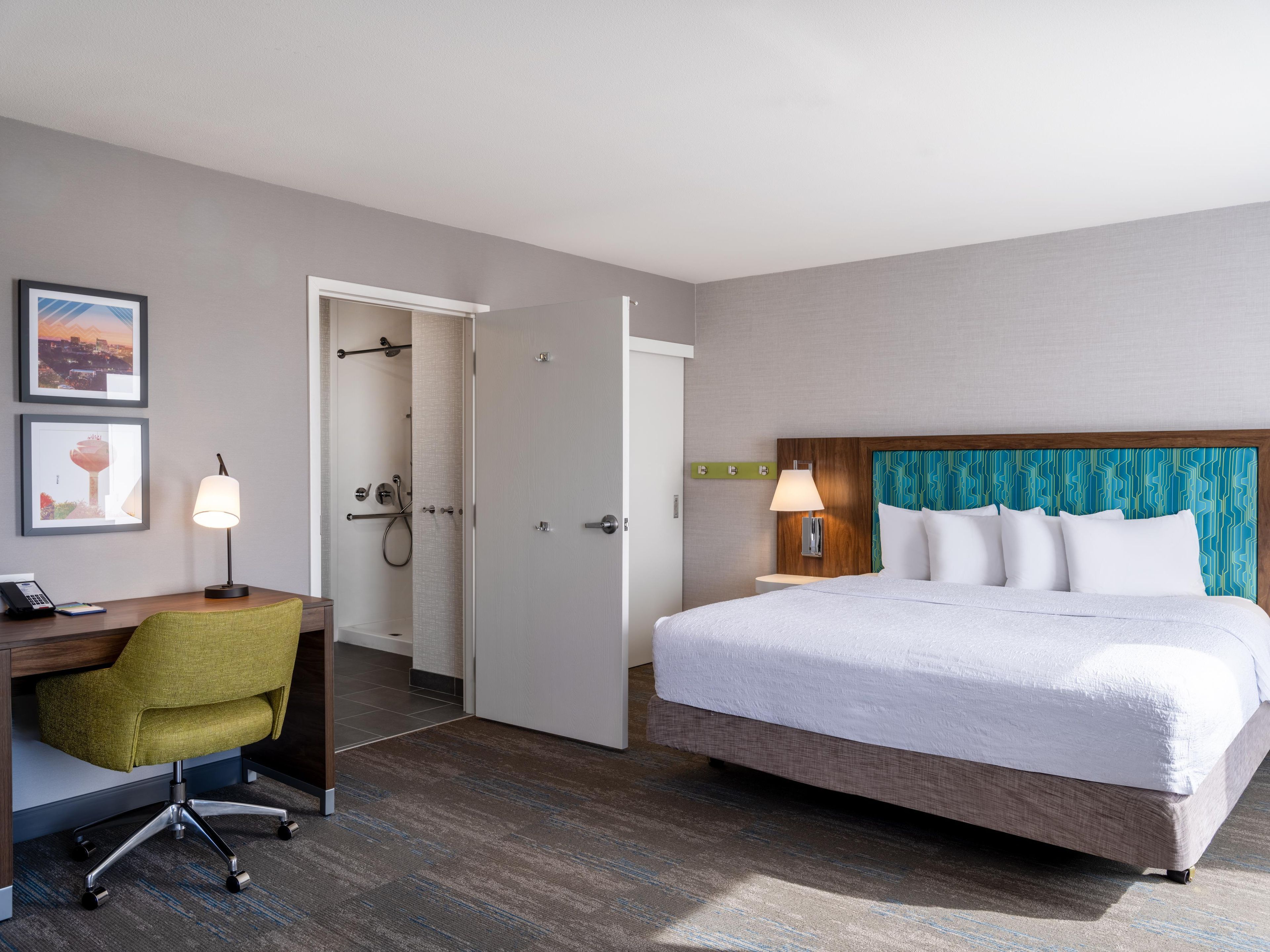 A hotel room with a bed, desk, chair, and a shower area.