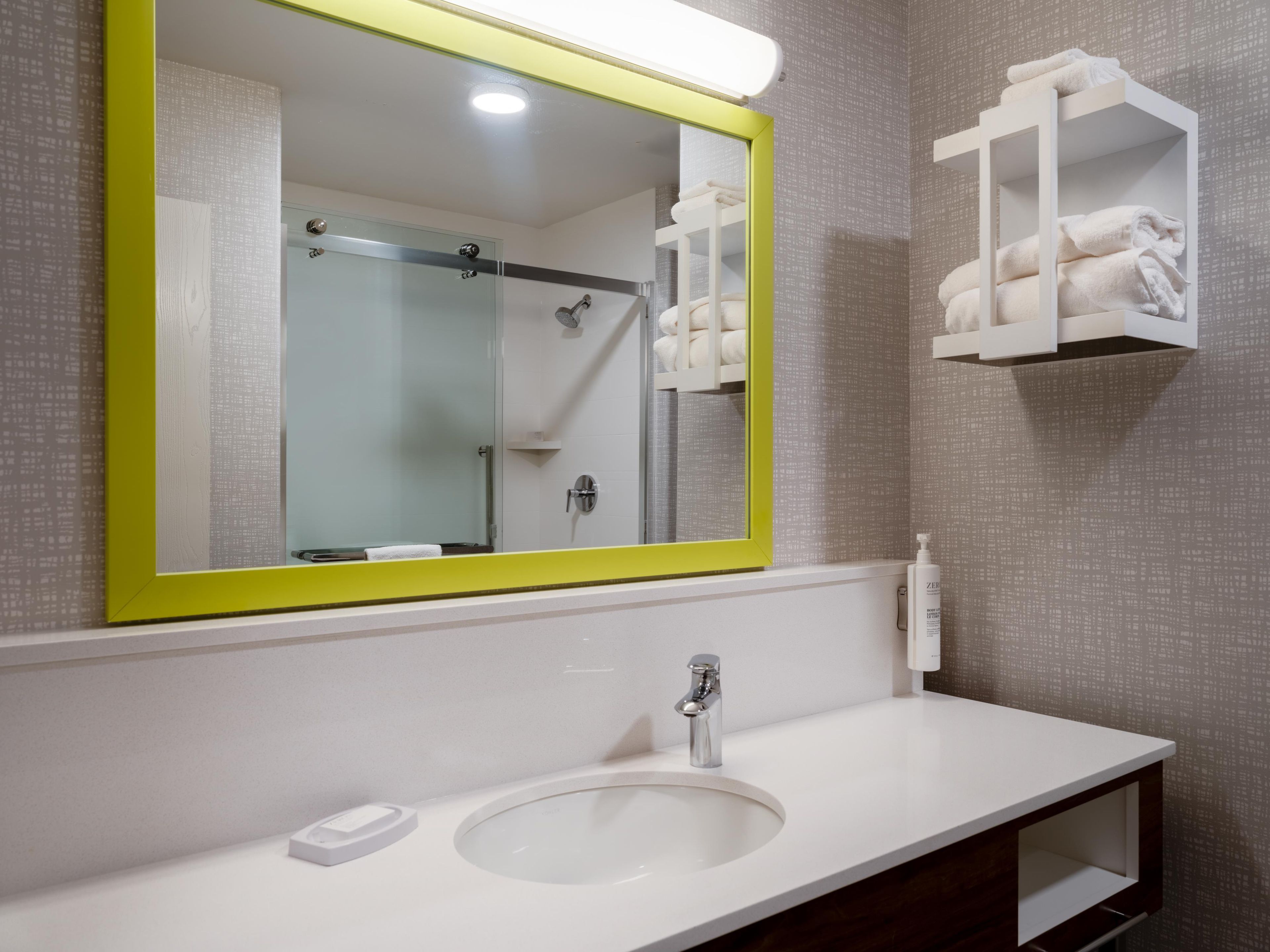 A bathroom with a white sink, a mirror with a yellow frame, and a towel rack with folded towels.