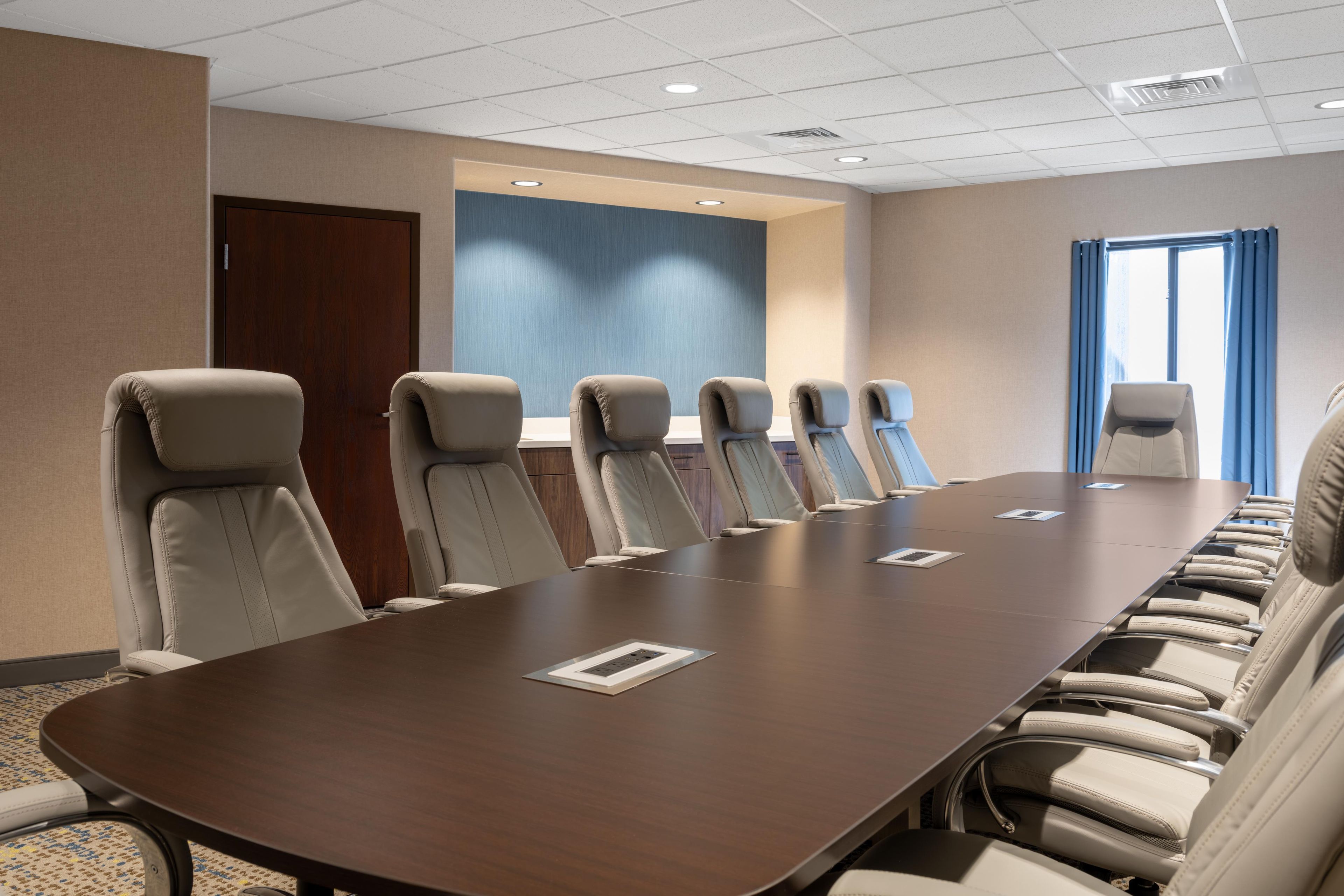 A conference room with a long table and multiple chairs, a wooden door, and a blue accent wall.