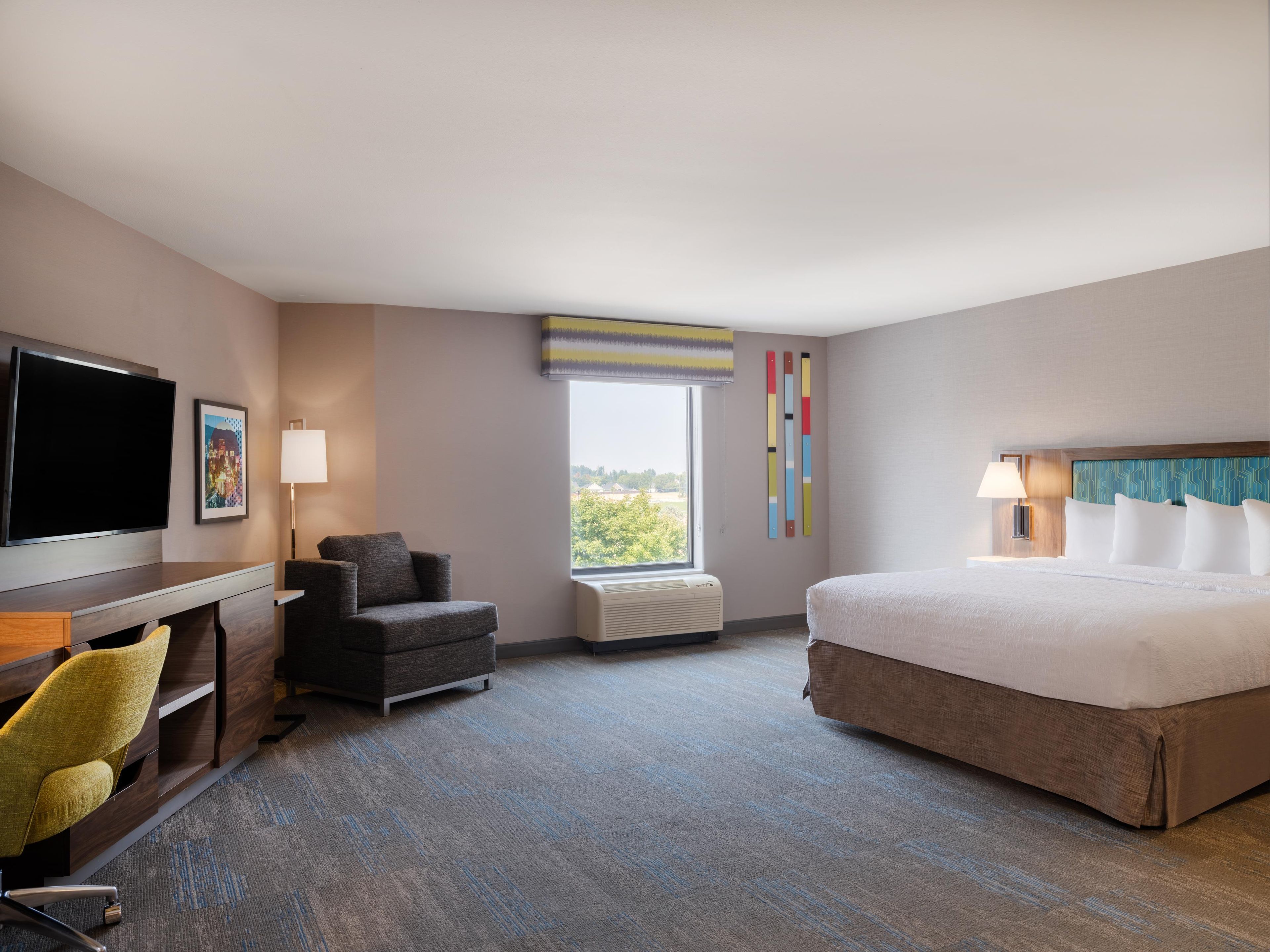 Habitación de hotel con una cama, un escritorio, una silla, un televisor y una ventana con vistas.