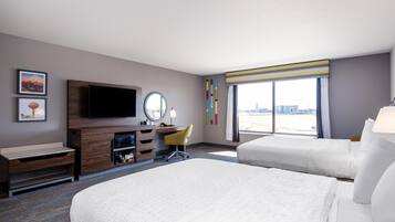 A hotel room with a large bed, a desk with a chair, a television, a mirror, and a window with a view of the city.