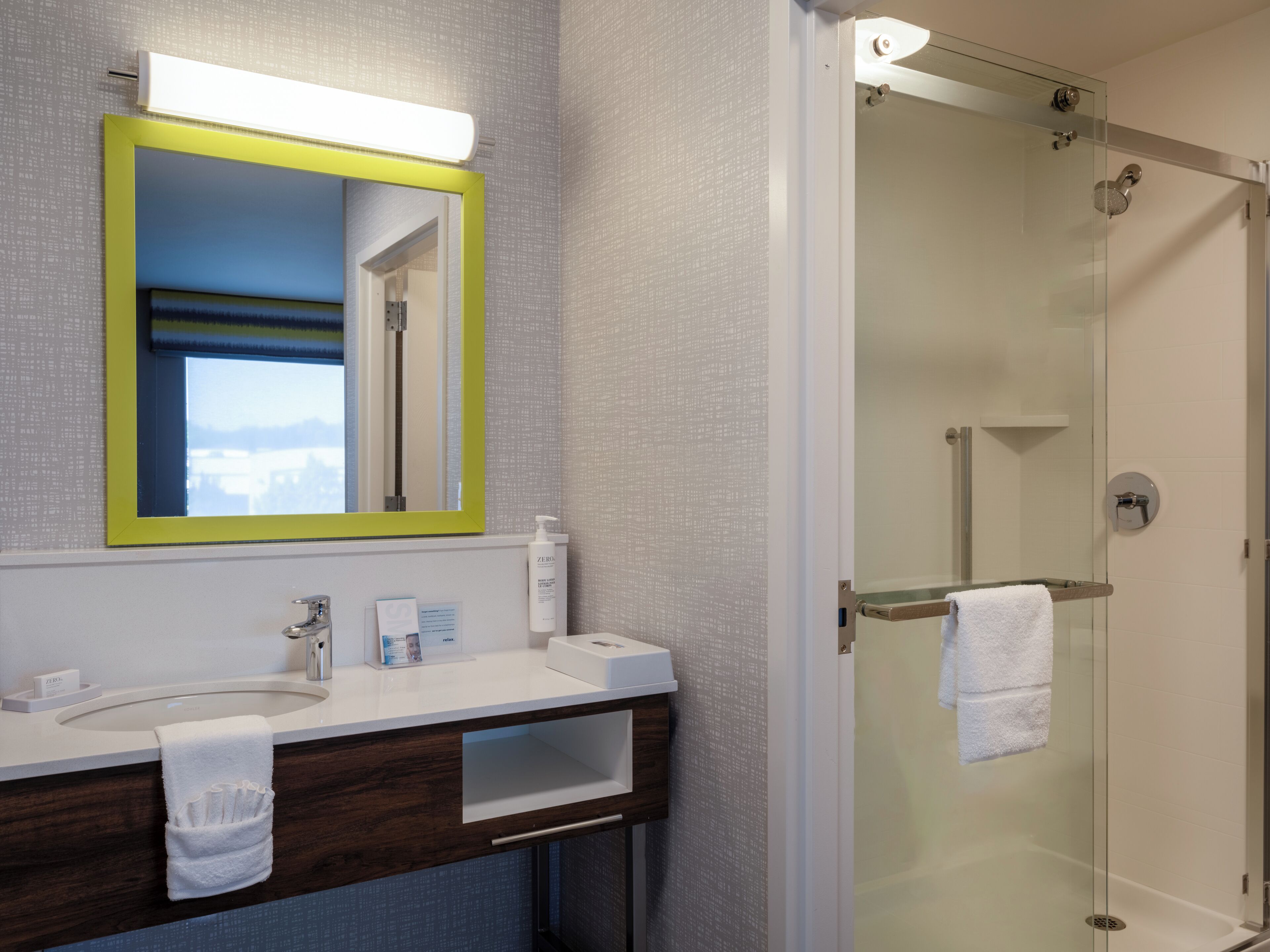 A modern bathroom with a large mirror, a sink, and a glass-enclosed shower.