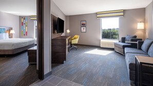 A modern hotel room with a bed, a desk, a sofa, and a large window offering a city view. - Hampton Inn & Suites Boise-Meridian (Meridian)