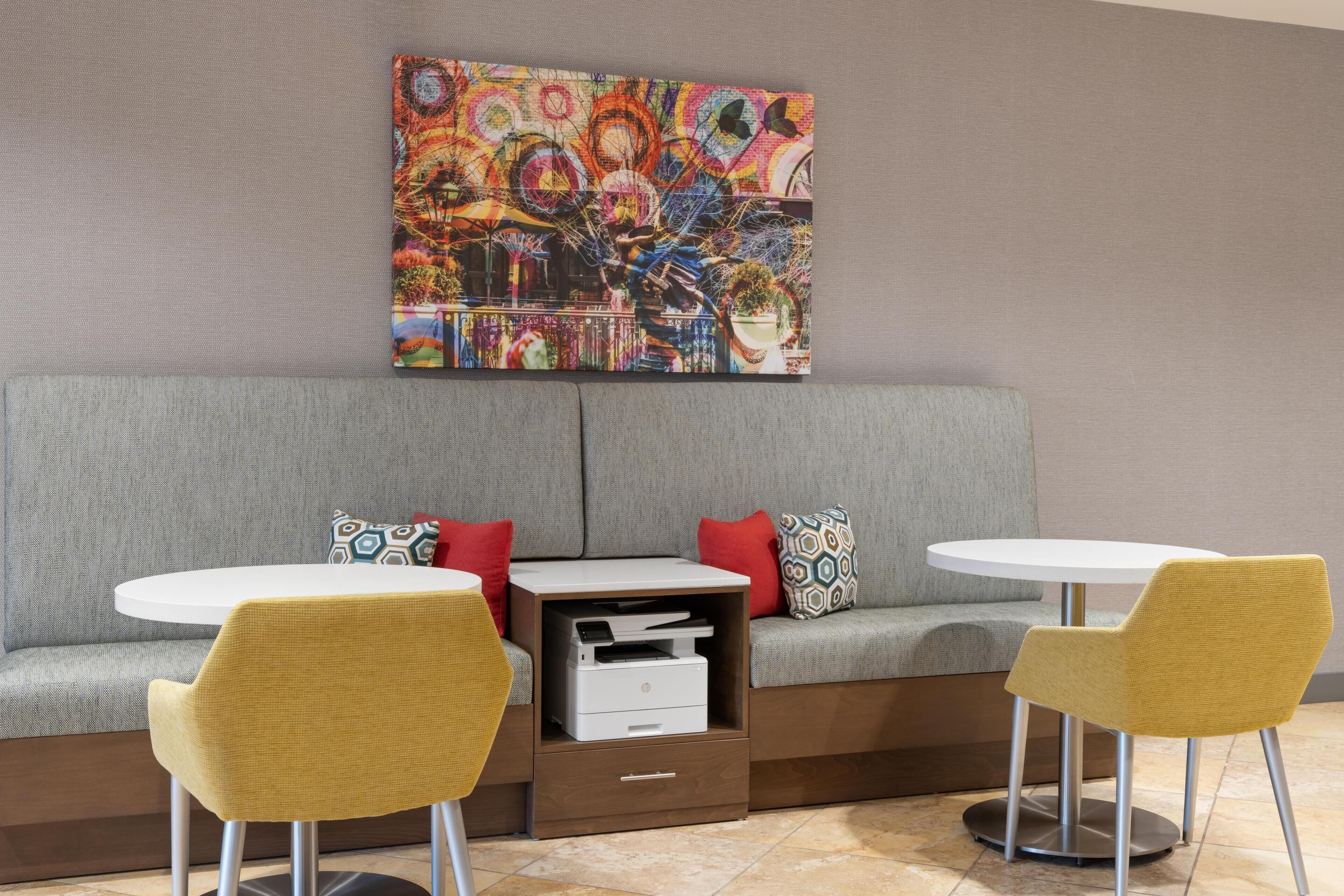 A modern room with a grey sofa, two yellow chairs, a white table, and a printer.