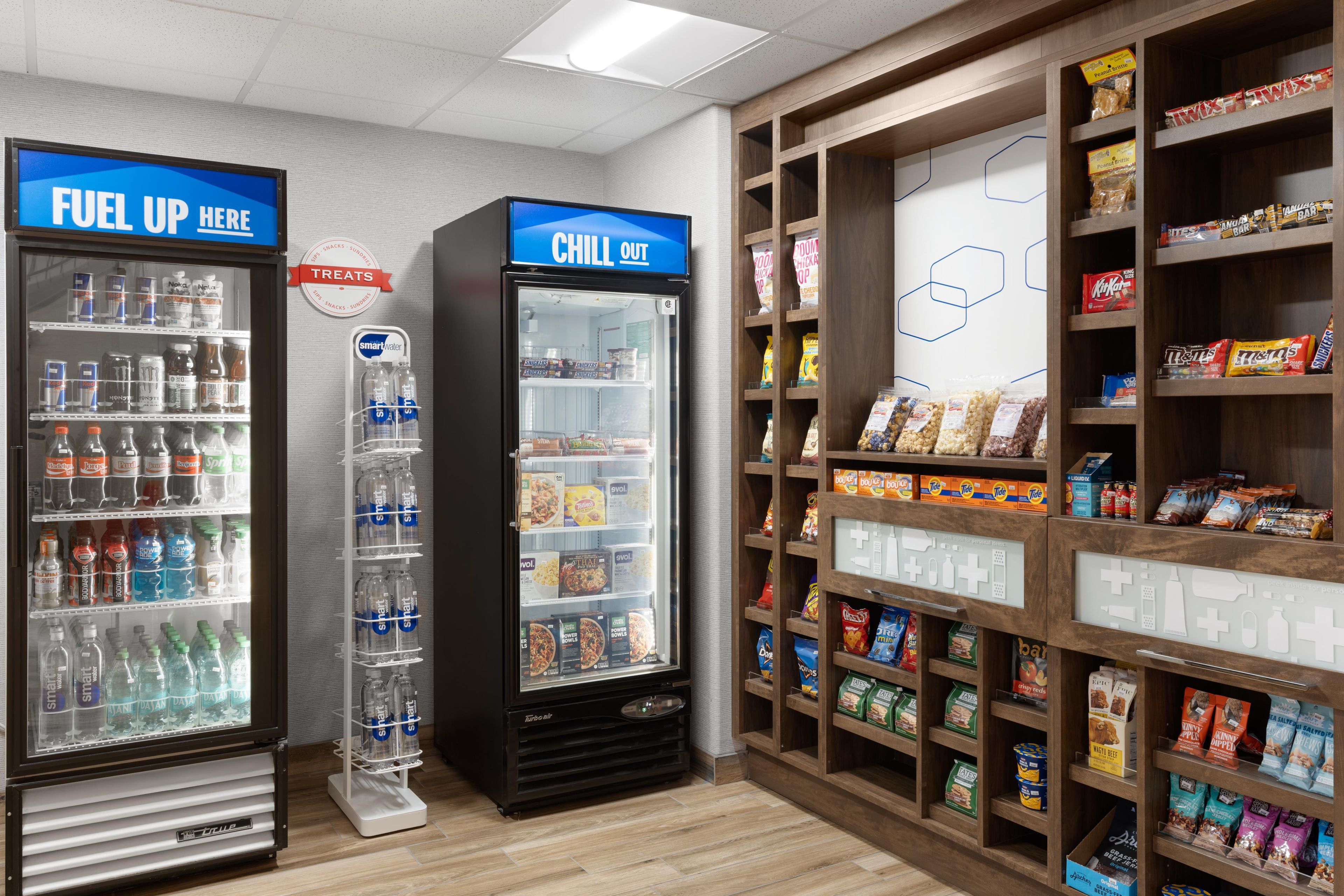 A section of a store with two refrigerated beverage dispensers labeled 'Fuel Up Here' and 'Chill Out,' stocked with various drinks and snacks.