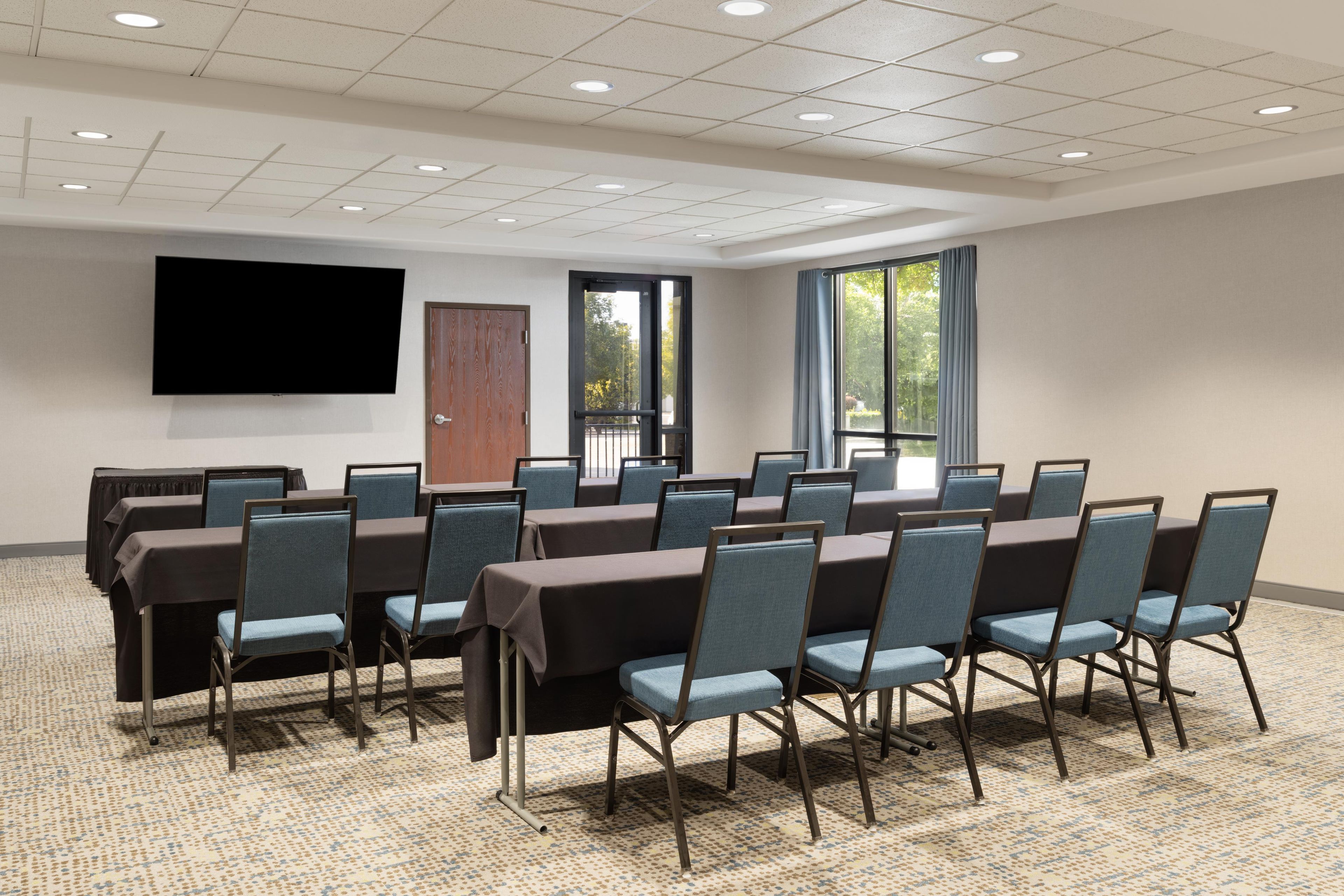 Una sala conferenze con una grande TV a schermo piatto, una porta e finestre con tende.