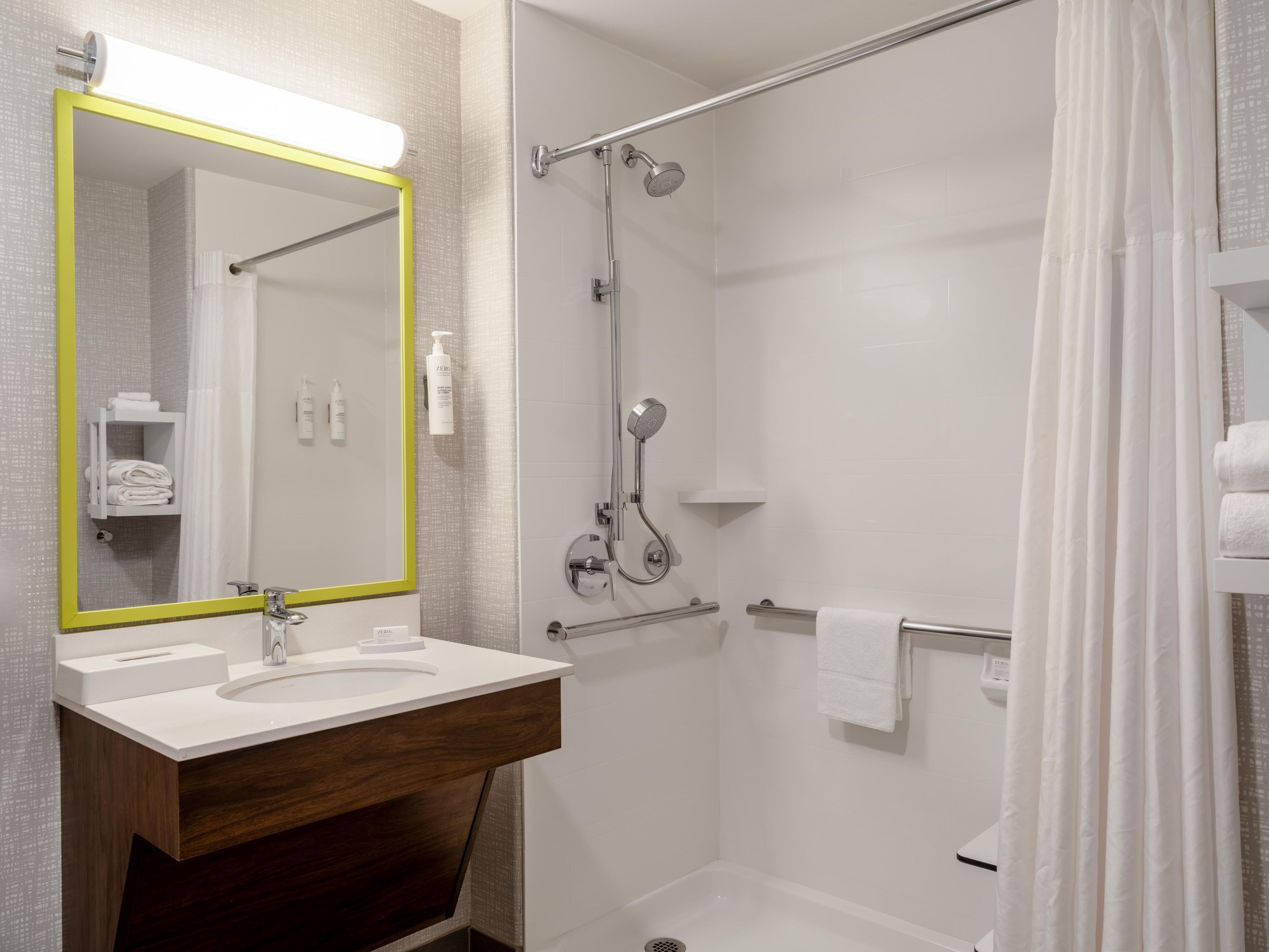 A bathroom with a mirror, sink, and shower.