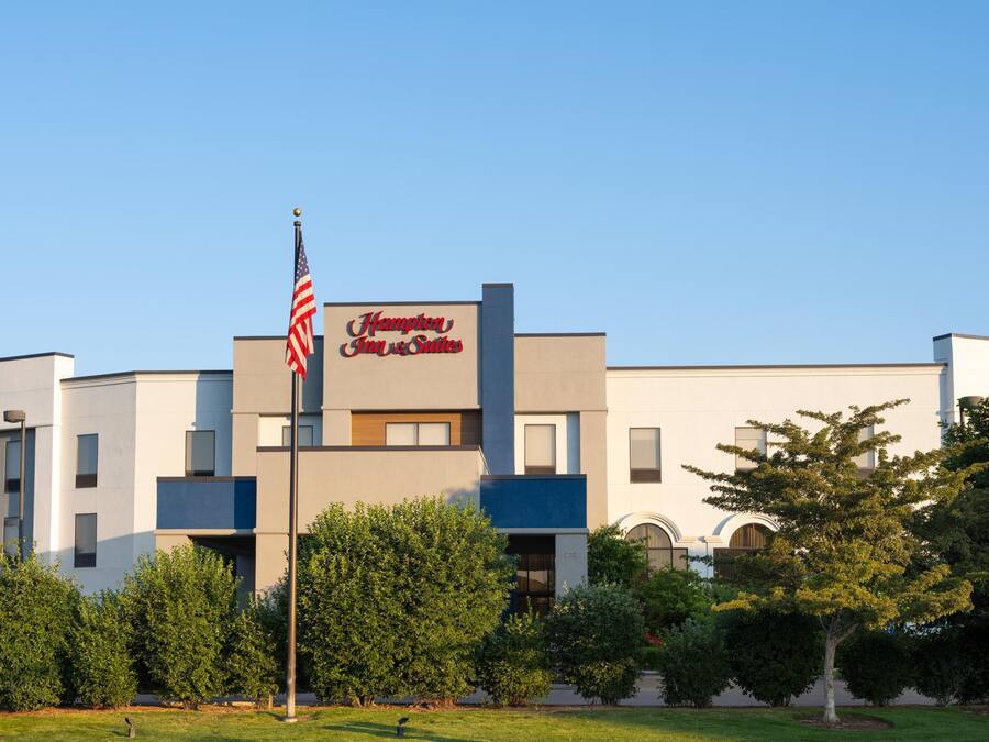 A Hampton Inn & Suites building with a flagpole, surrounded by greenery.