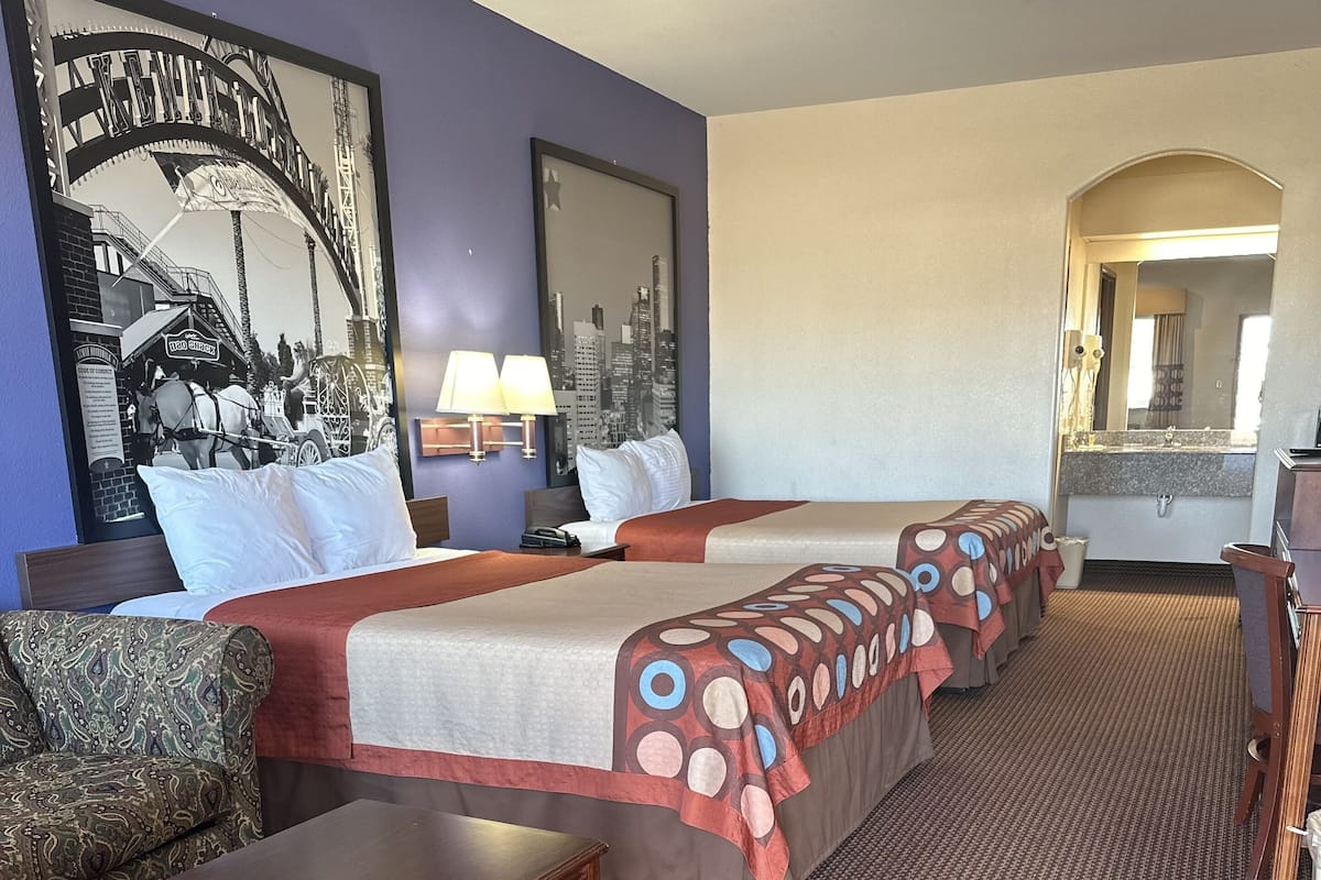 Une chambre d’hôtel avec un grand lit, un bureau, une chaise et une salle de bain visible à travers une porte en arc de cercle.