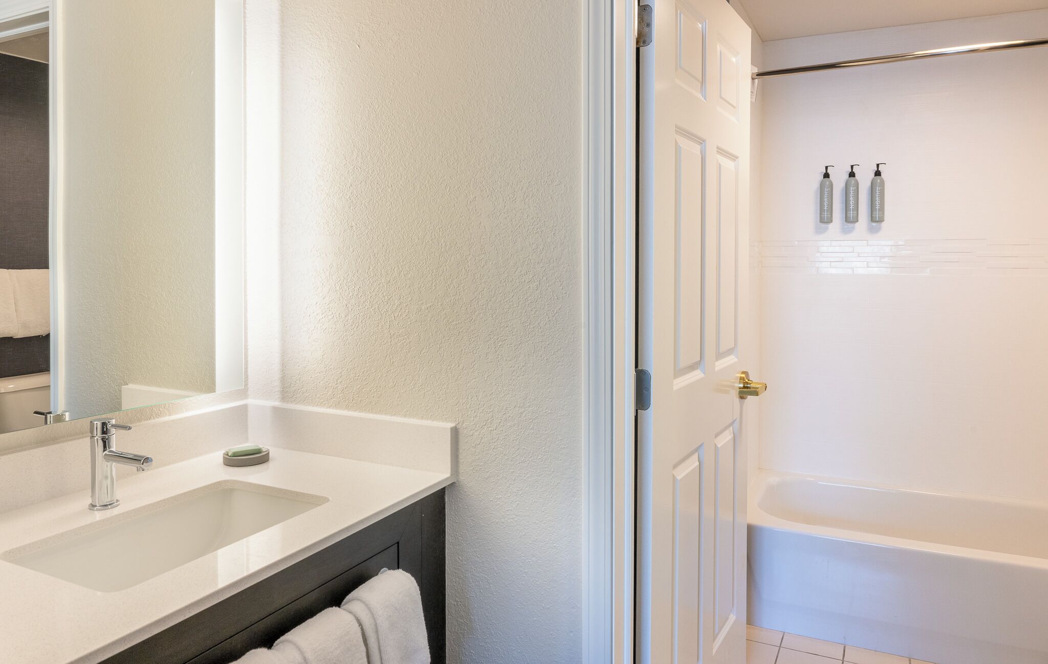 A bathroom with a large mirror, a sink, a towel rack, and a shower area with toiletries.