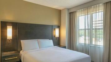 A hotel room with a large bed, two bedside tables, and a window with sheer curtains.
