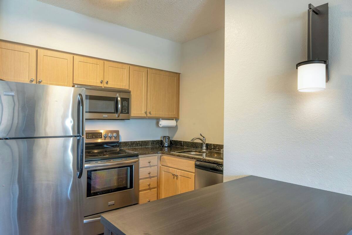 A modern kitchen with stainless steel appliances, wooden cabinets, and a granite countertop.