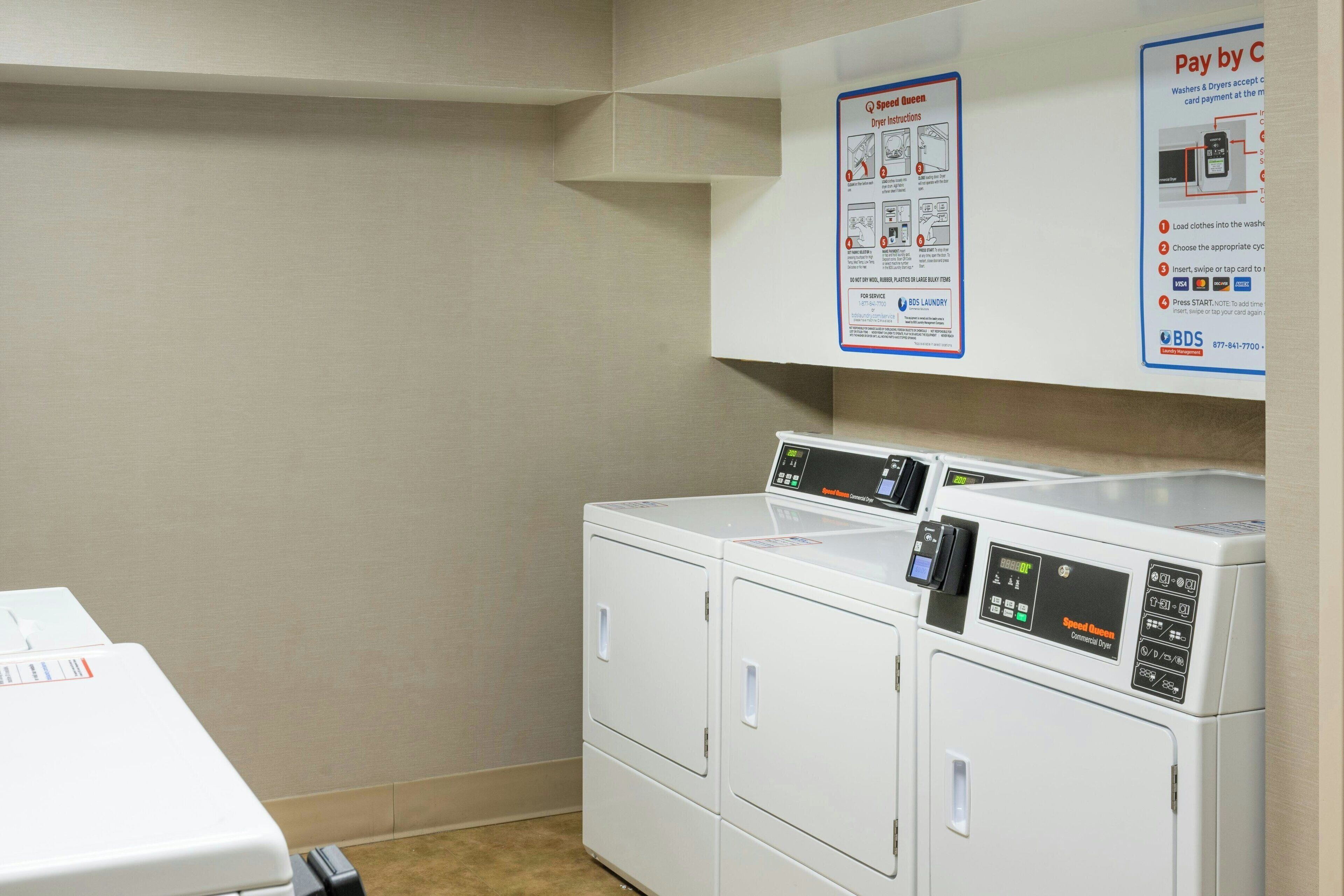 A laundry area with a washing machine and dryer, a wall-mounted instruction poster, and a table with a white box.