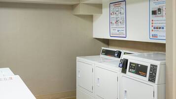 A laundry area with a washing machine and dryer, a wall-mounted instruction poster, and a table with a white box.