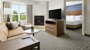 Habitación de hotel con sofá, televisión, chimenea, cama y vista a zonas verdes.