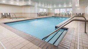 Una piscina interior con suelo de baldosas, un jacuzzi y varias sillas de descanso.