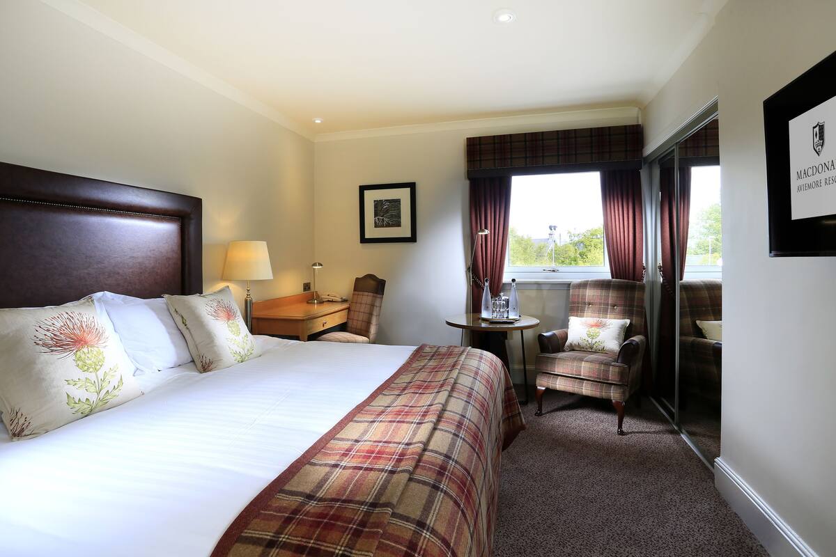 A hotel room with a large bed, a desk, a chair, and a window with curtains.